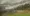 Scenery of the mountain and field outside, from the train window, with rain droplets running down.